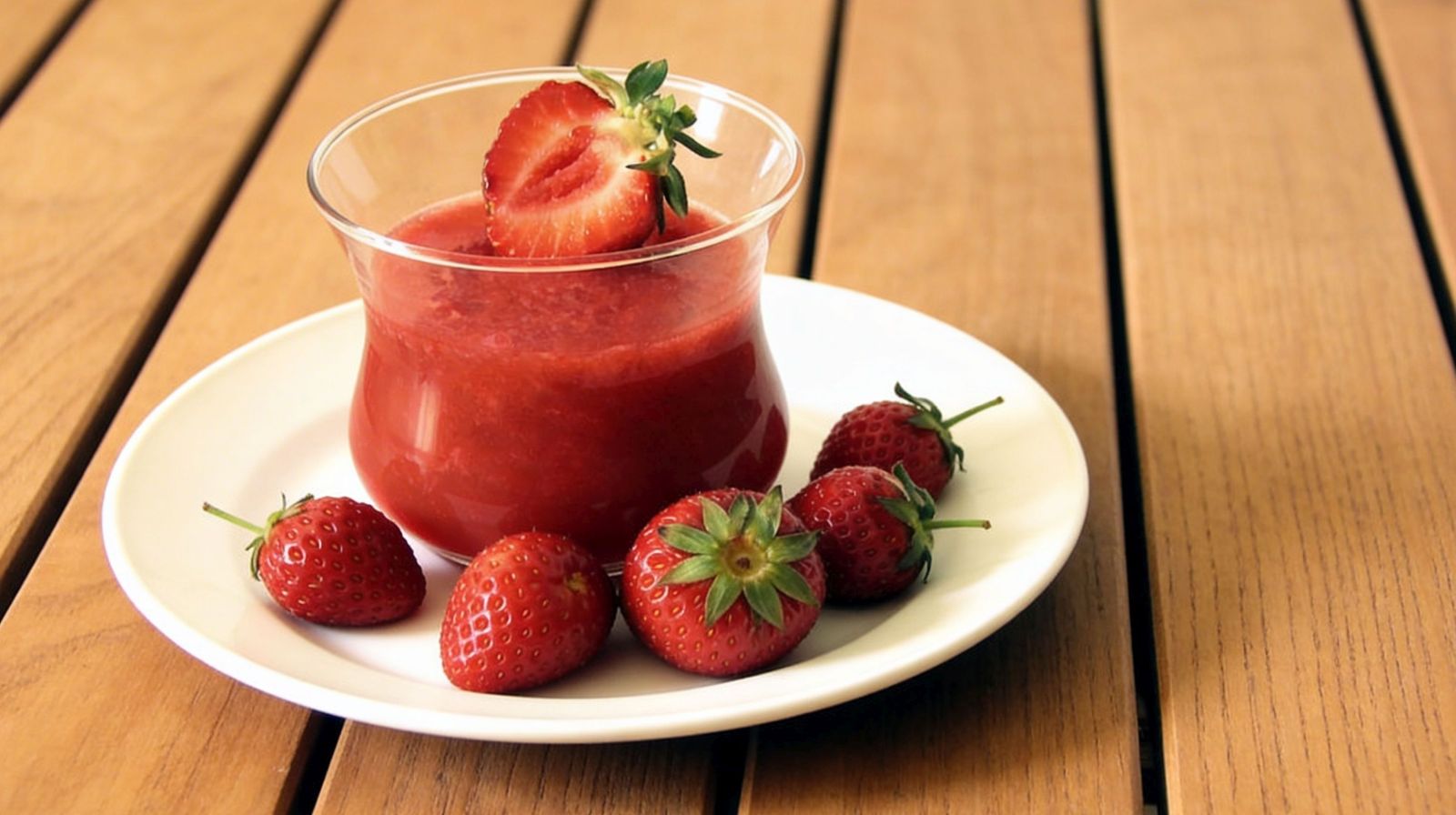 Domowa galaretka truskawkowa z prawdziwych owoców w szklanym pucharku, świeże truskawki na białym talerzu.