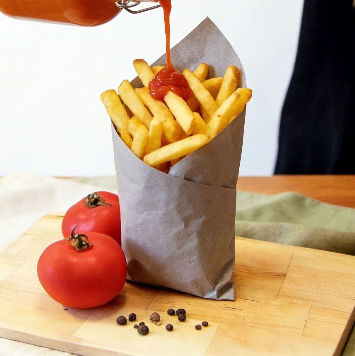 Domowy ketchup z pomidorów polewany na chrupiące frytki, podany w papierowej tutce na drewnianym blacie.
