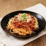 Spaghetti bolognese z mięsnym sosem pomidorowym, startym parmezanem i świeżą bazylią na czarnym talerzu.
