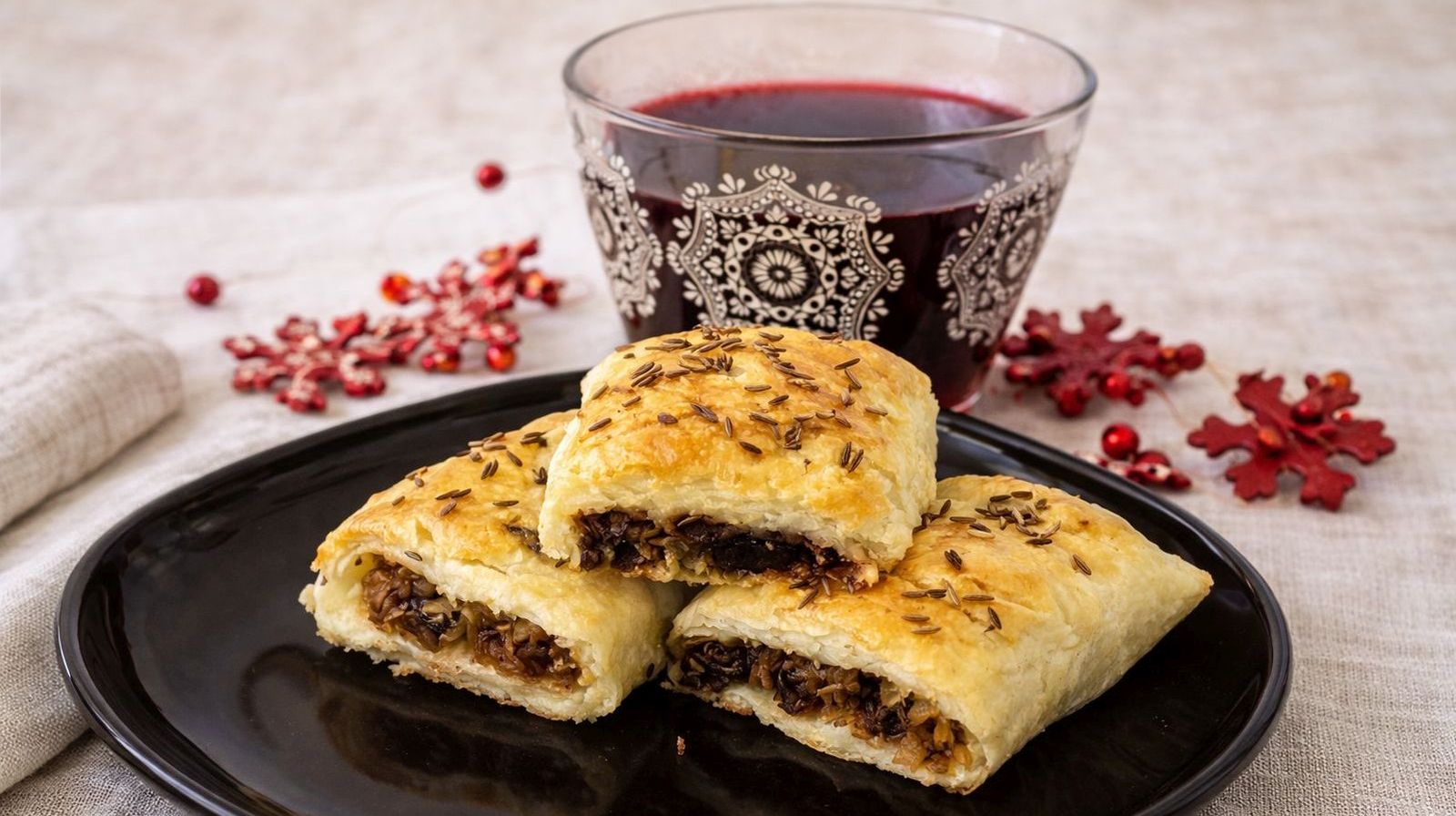 Błyskawiczne kapuśniaczki z ciasta francuskiego z kapustą i grzybami podane na czarnym talerzu z czerwonym barszczem.