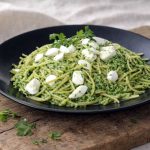 Makaron z pietruszkowym pesto i mozzarellą – spaghetti z zielonym pietruszkowym pesto i kawałkami sera na czarnym talerzu.