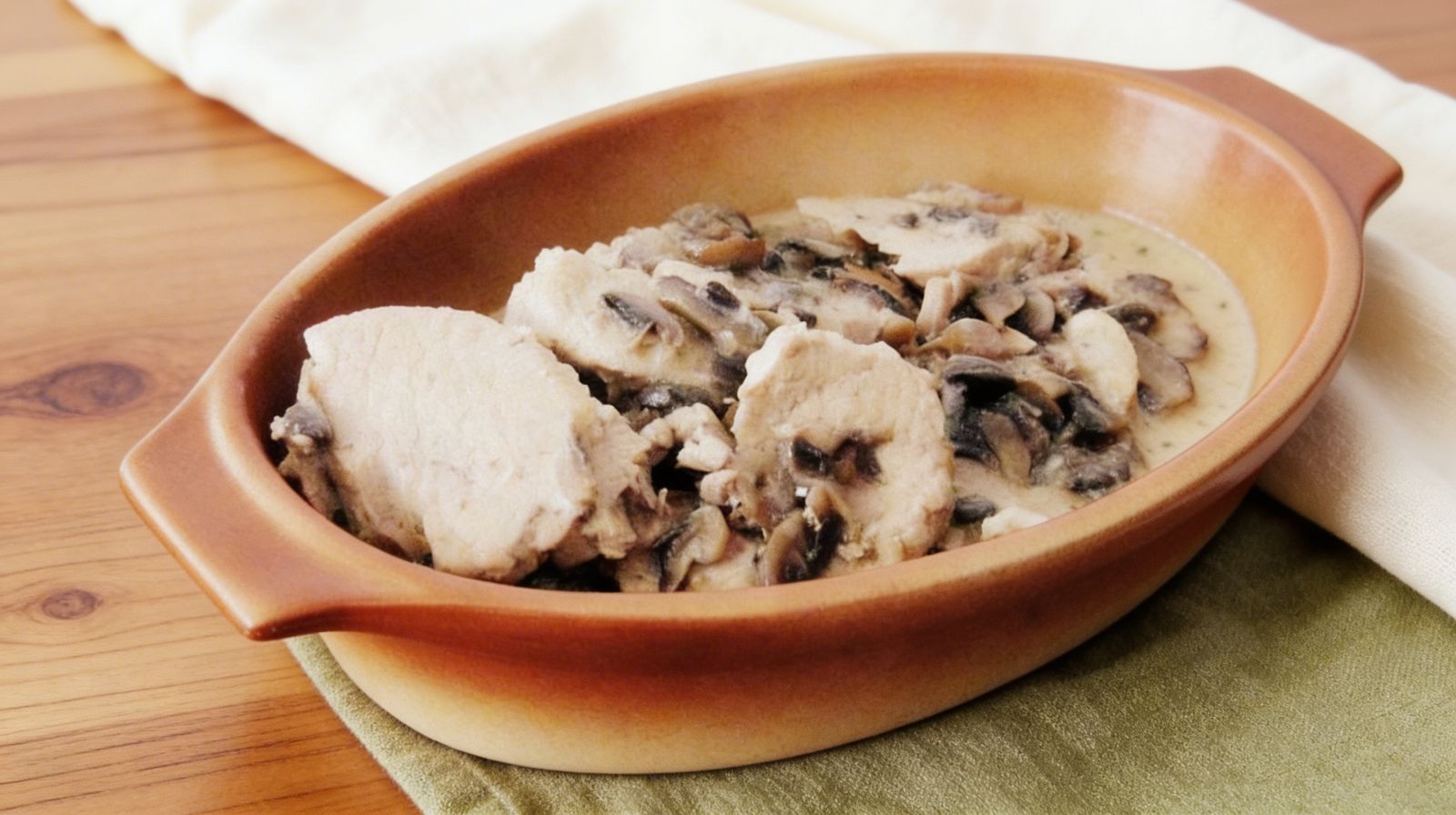 Schab duszony w pieczarkach w kremowym sosie śmietanowym podany w kamiennym naczyniu, miękkie plastry schabu z dużą ilością pieczarek.