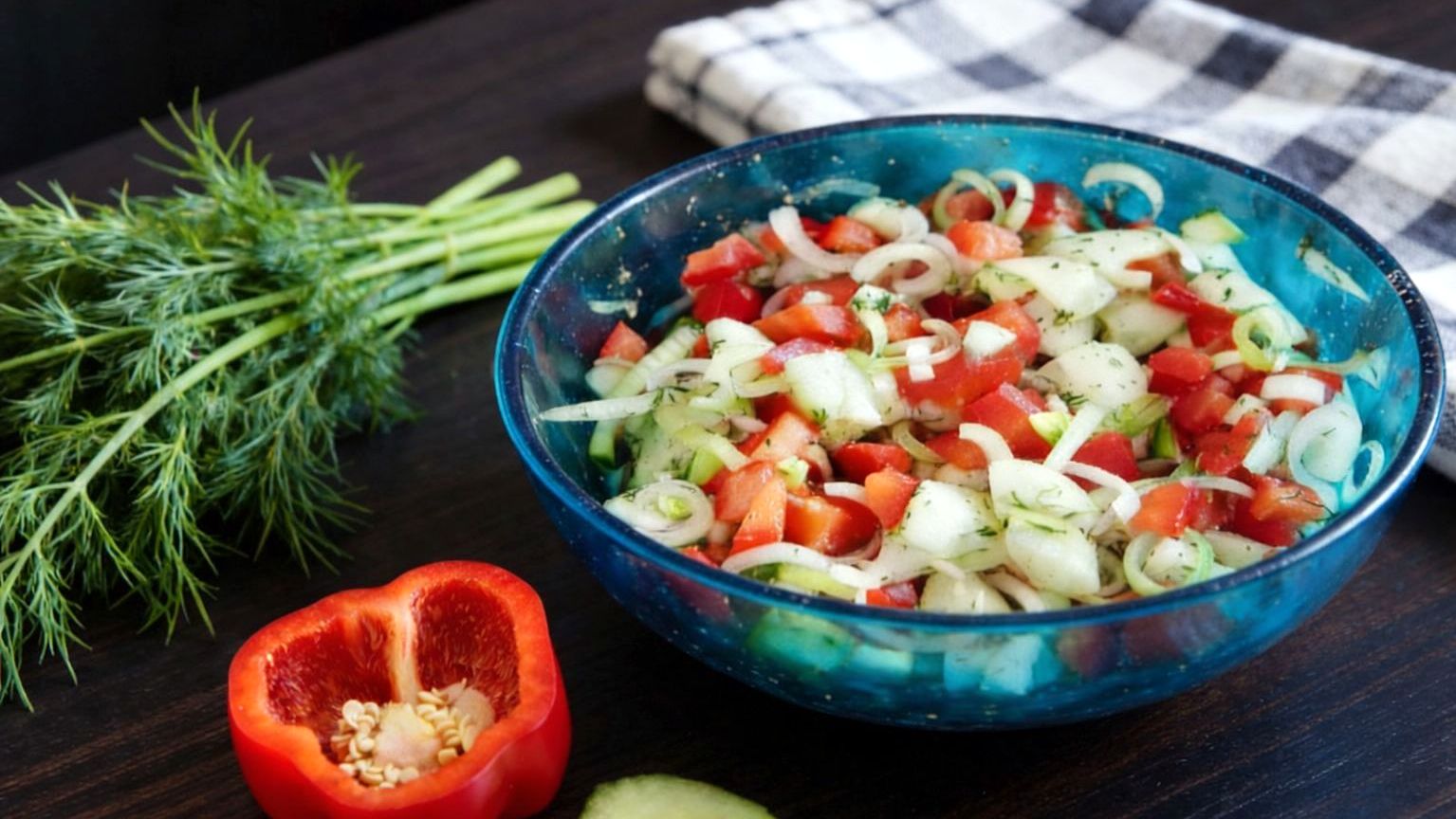 Surówka paprykowo-ogórkowa z porem w niebieskiej misce, z koperkiem obok, na drewnianym stole.