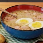 Żurek tradycyjny z białą kiełbasą i jajkiem na twardo w niebieskiej misce, podany z chrzanem i ziemniakami.